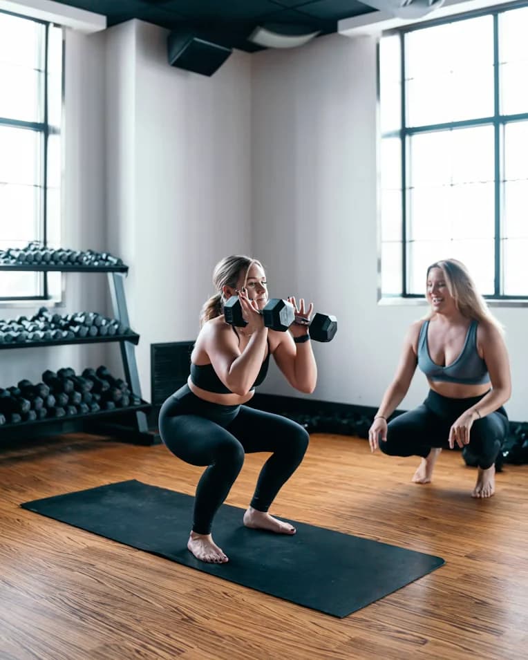 A coach crouching beside a client doing a dumbbell squat